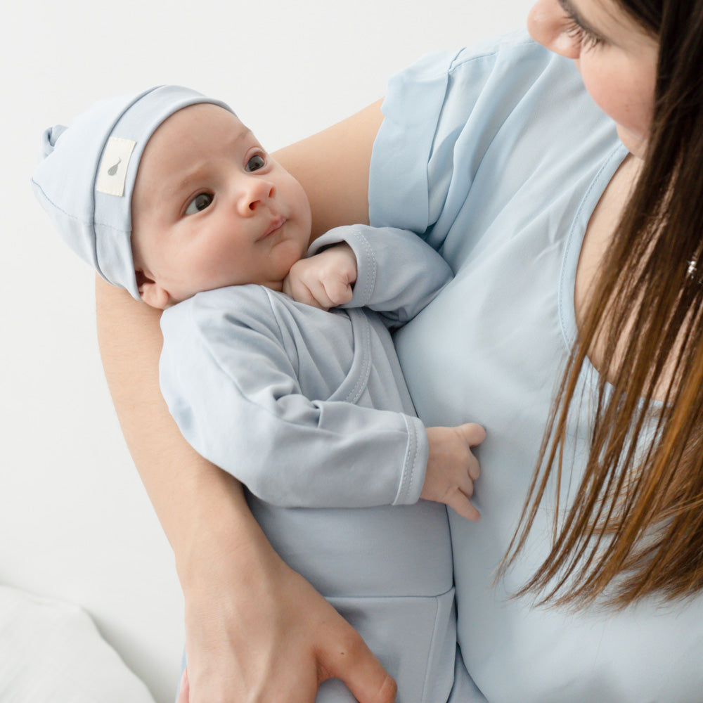 Mamá cargando a su bebé con pañalero y gorrito azul de Mae & Mini